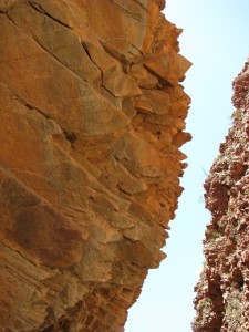 Looking up at two overhanging rock faces: one, red sandstone; one, red coglomerate.