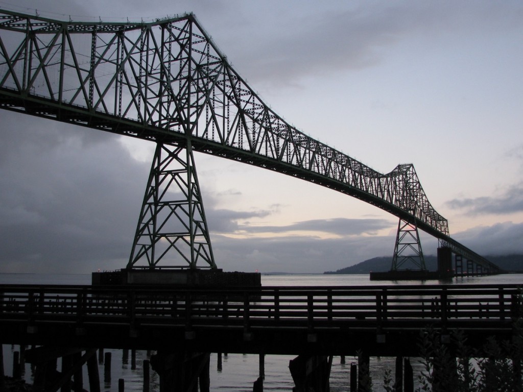 Late afternoon silhouette of metal bridge across Columbia River; wooden walkway in foreground.