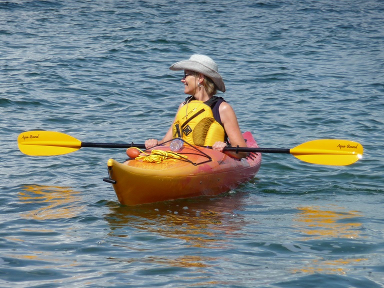 Red and yellow kayak; woman sitting therein, on bright, sunny day.