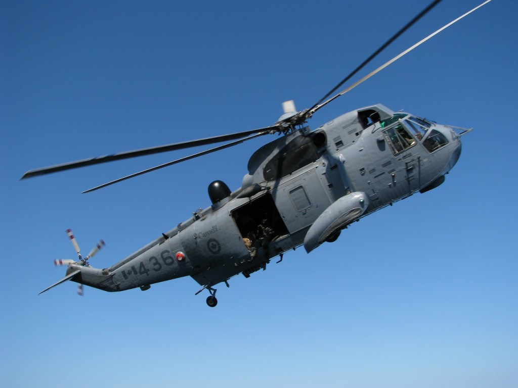 Natural close-up of airborne military helicopter from deck of Canadian frigate.