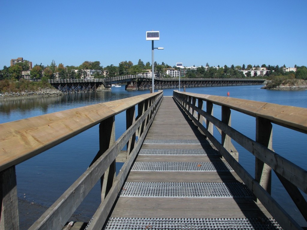 Wooden pier extends out into harbour; background shows wooden bridge over inlet.