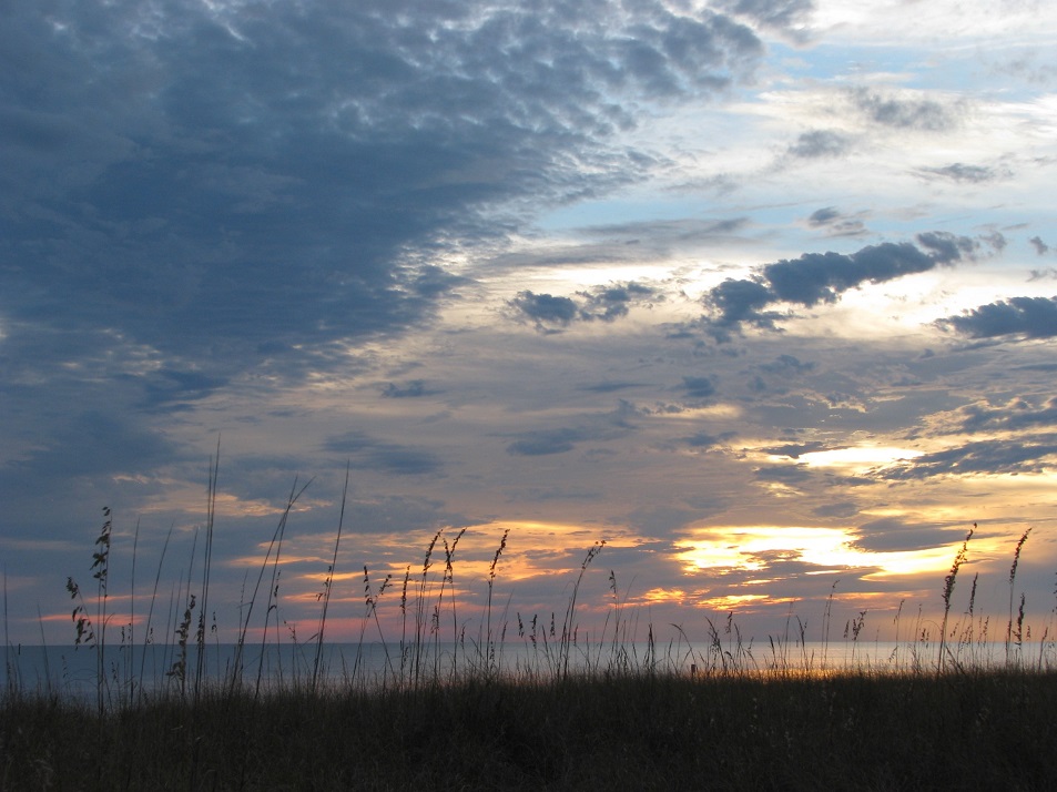 Grassy sand dune in foreground, Gulf of Mexico in background; sunset filling most of the photo.