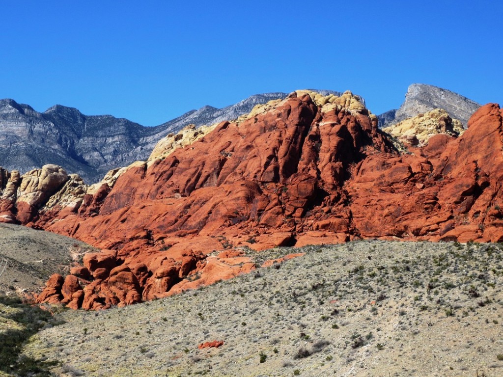 Successive layers of red, beige and purple rock, with scrub desert in foreground.