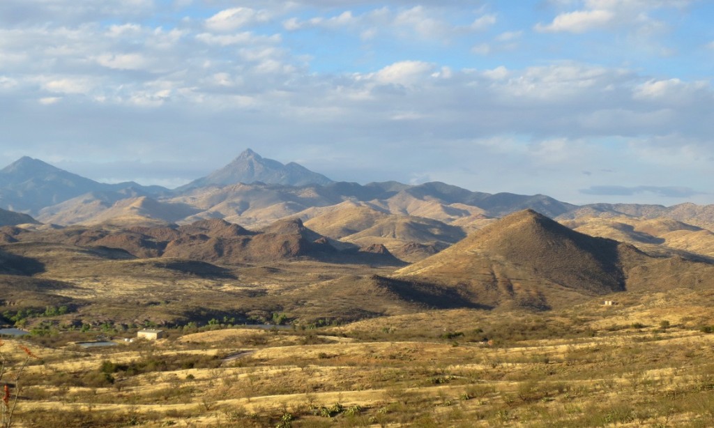 Late afternoon light on foothills rising to mountains; cloud-hazed sky.