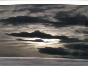 Almost black and white rendering of cloudy sky reflected in minivan window.