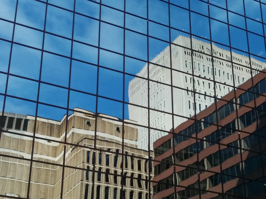 Three office buildings of different sizes and colours reflected in a fourth