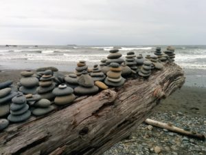 Smooth stones piled up on driftwood log on beach.