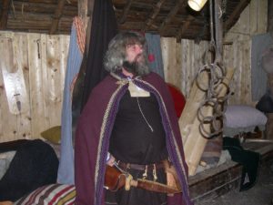 Actor in period dress in reconstructed Norse settlement.