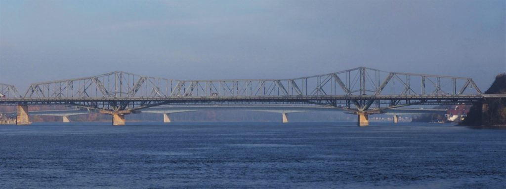 Ground-level view of Alexandra Bridge in distance, centered over Ottawa River.
