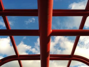Red metal beams of bus shelter roof; showing blue sky through the plexiglass.