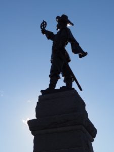 Silhouetted statue of Samuel de Champlain, against a blue sky.