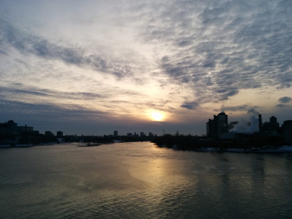 Silhouetted buildings on riverbank at sunset.