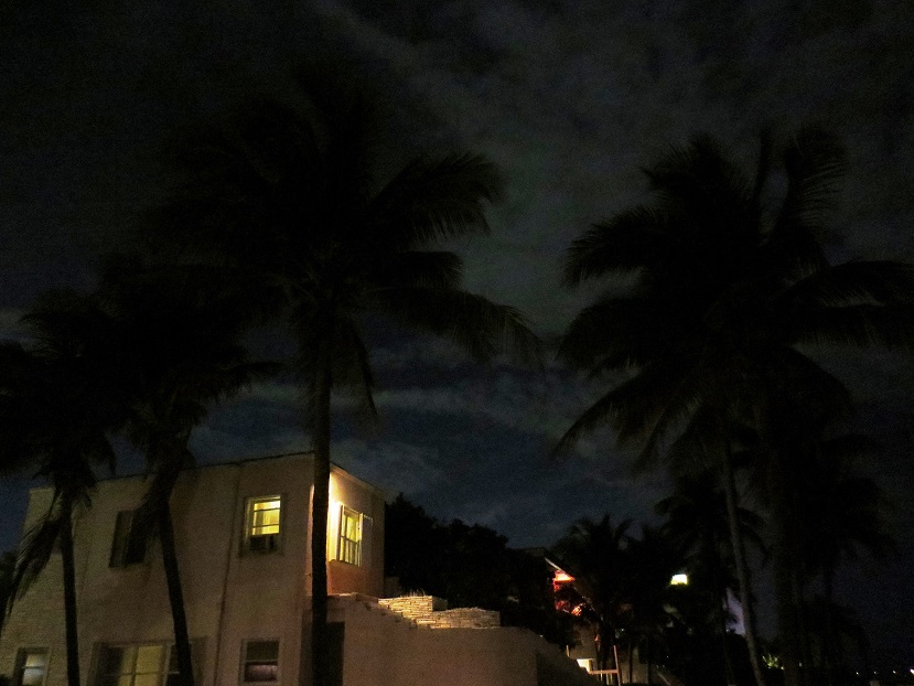 Night scene of stucco, two-storied hotel with palm trees.