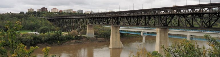 Trestle rail bridge across muddy North Saskatchewan River.
