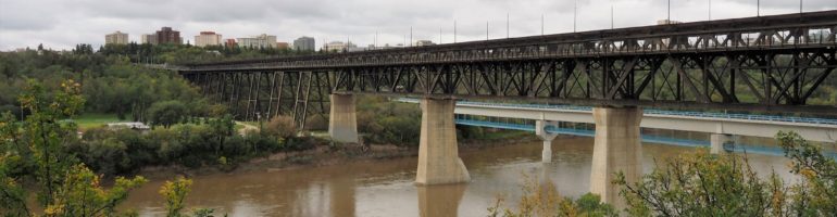 Trestle rail bridge across muddy North Saskatchewan River.