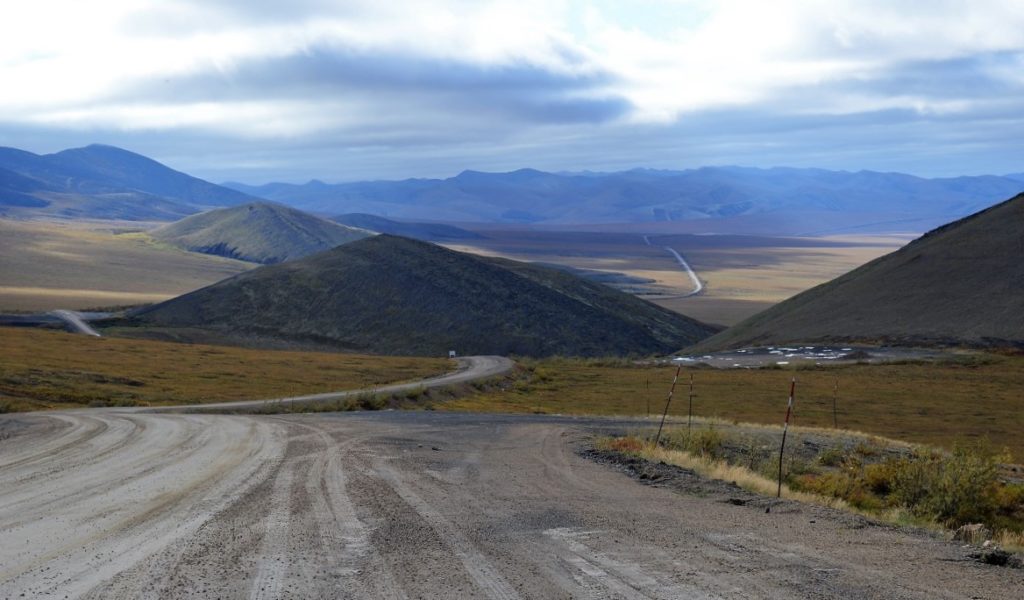 Gravel roadbed of Dempster Highway snaking around hills an d disappearing into the mountain range on the horizon.