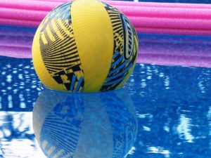 Blue and yellow ball floating in pool, flanked by pink noodle.