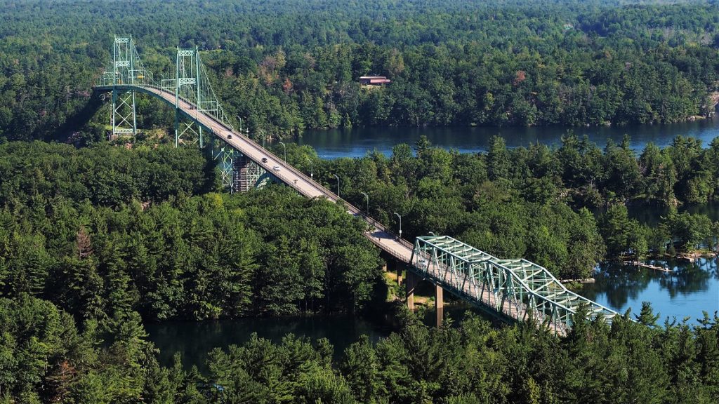Minty-green bridge (drive-through truss and cable-stayed) snaking through dark-green trees.