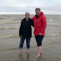 Two people in parkas standing barefoot in Arctic Ocean.