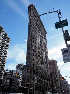 View of iconic Flatiron Building from street corner, with stree lights and signs in the way.