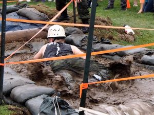 Recruit belly-crawling through muddy water in ditch.