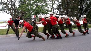 Recruits at 45 degree angle to road, pulling rope attached to truck.