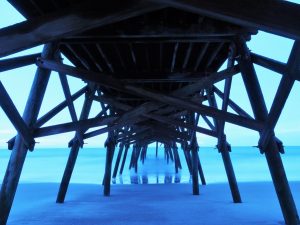 Surreal view of layers of blue - sand, water, sky - under wooden pier at dawn.