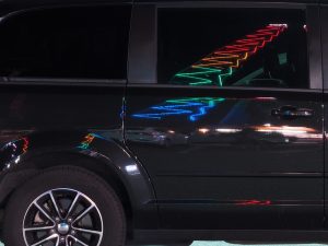 Illuminated tower reflected in side panel and window of balck SUV at night.