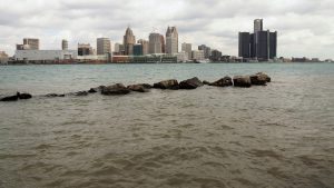 Shore-level view of Detroit River and city skyline at mid-day.