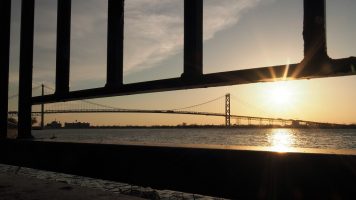 Ambassador Bridge at sunset, trhough railing along riverwalk