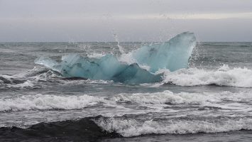 Blue iceberg in surf off black basalt beach